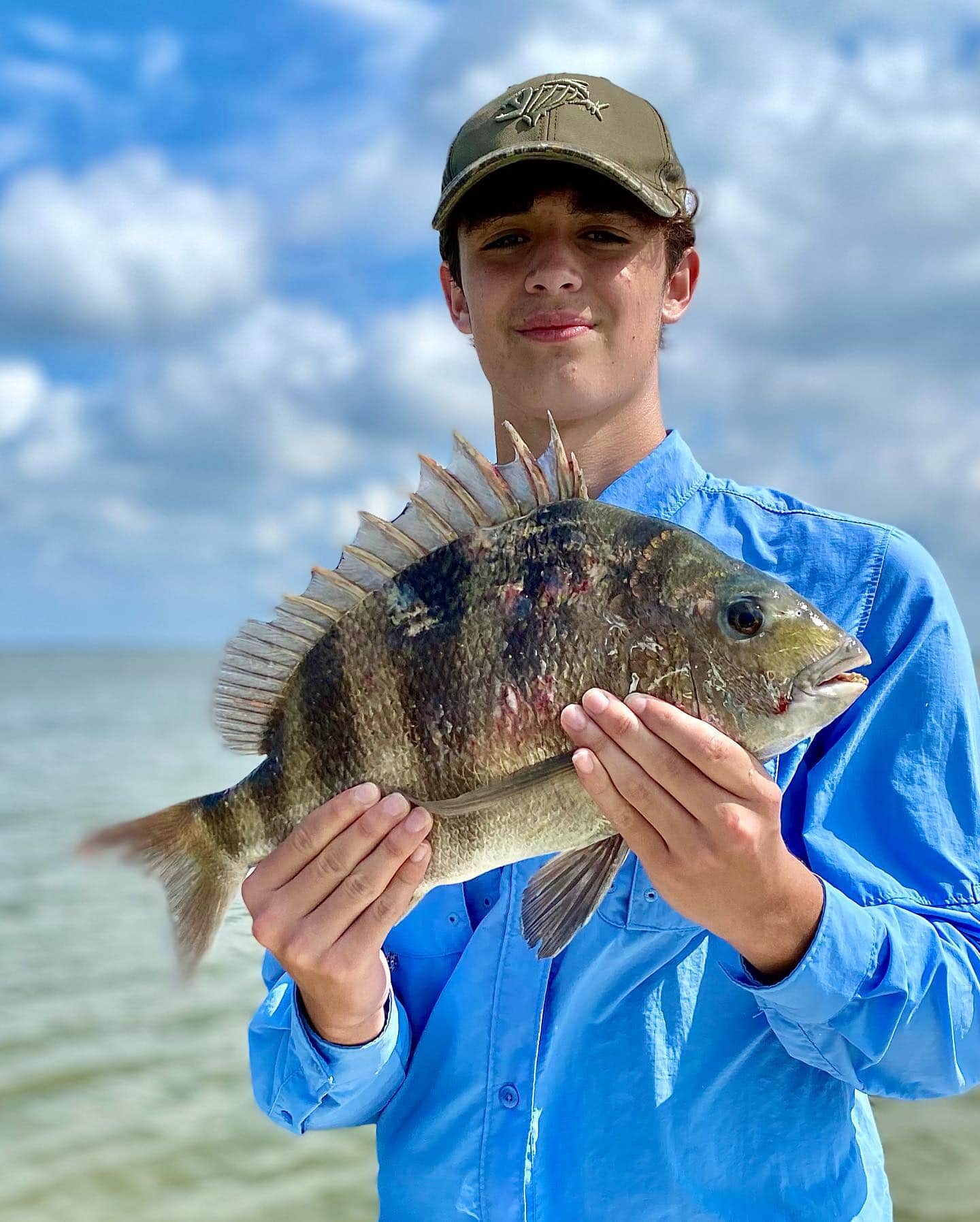 Young man holding up a sheepshead he caught on a fishing charter in Delacroix.