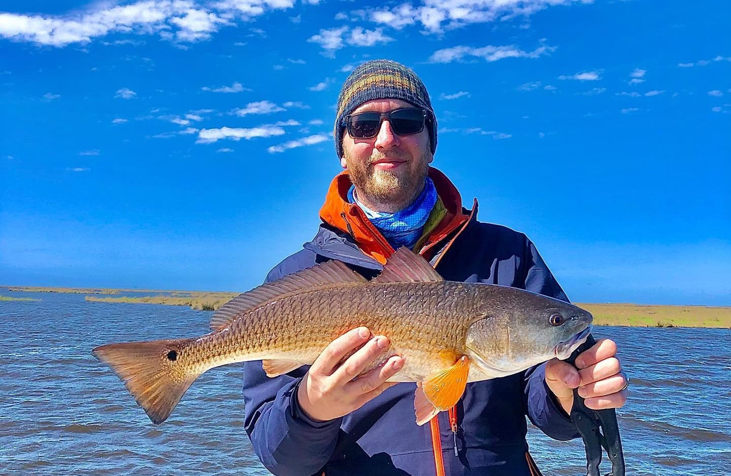 Man holding up a redfish he caught while on a fishing charter in Delacroix during the fall.