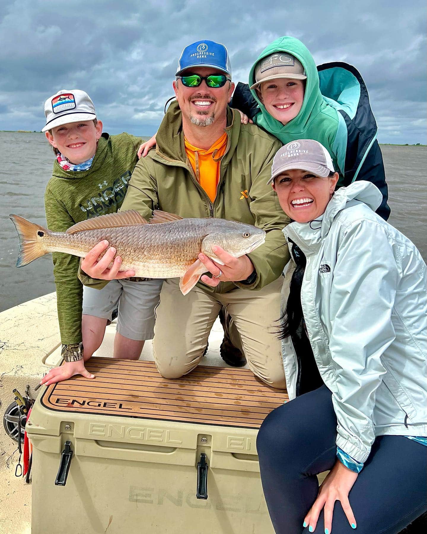 Family on a fishing boat holding up a fish and smiling.