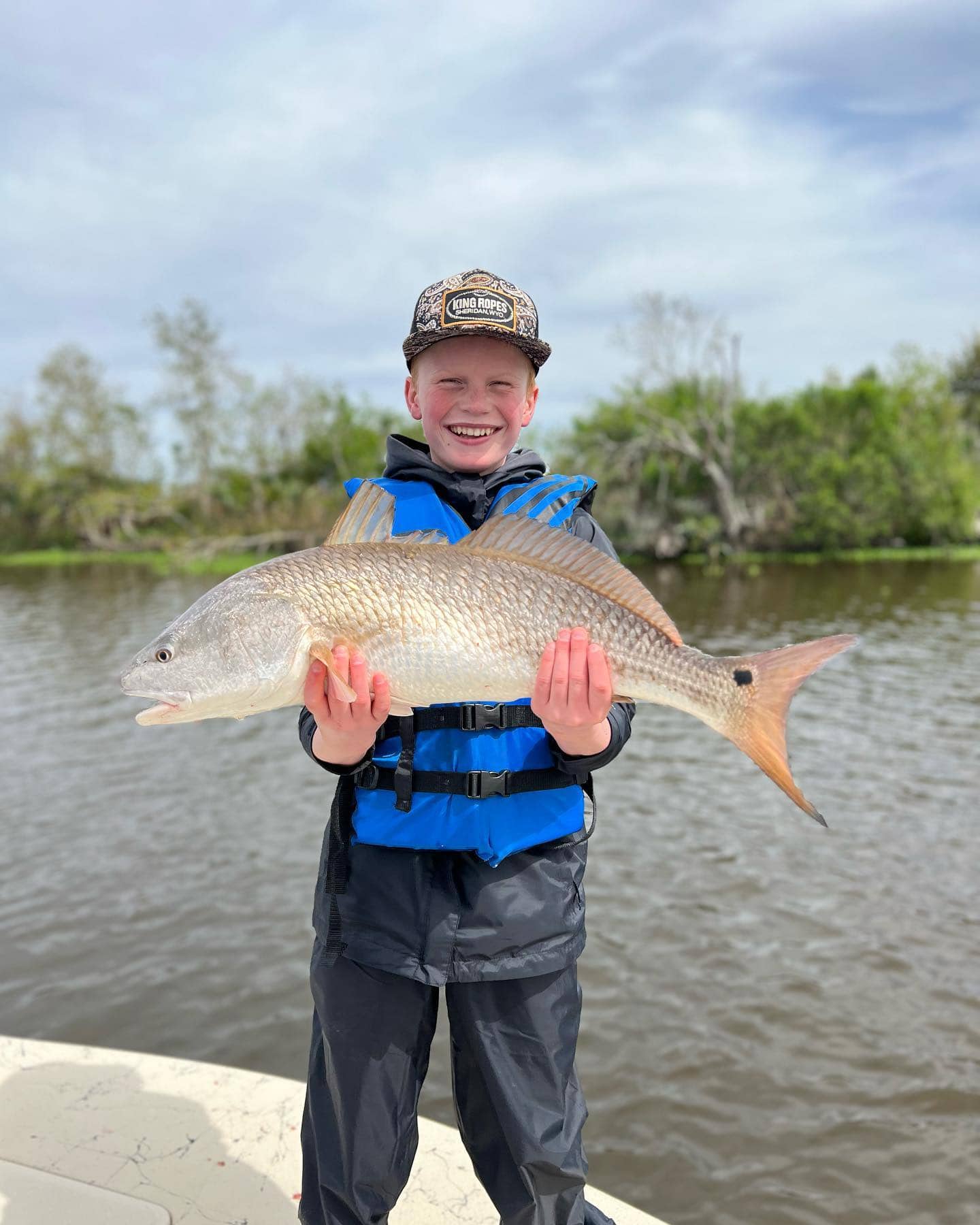 A young boy holding up a redfish he caught while on a family-friendly fishing charter.