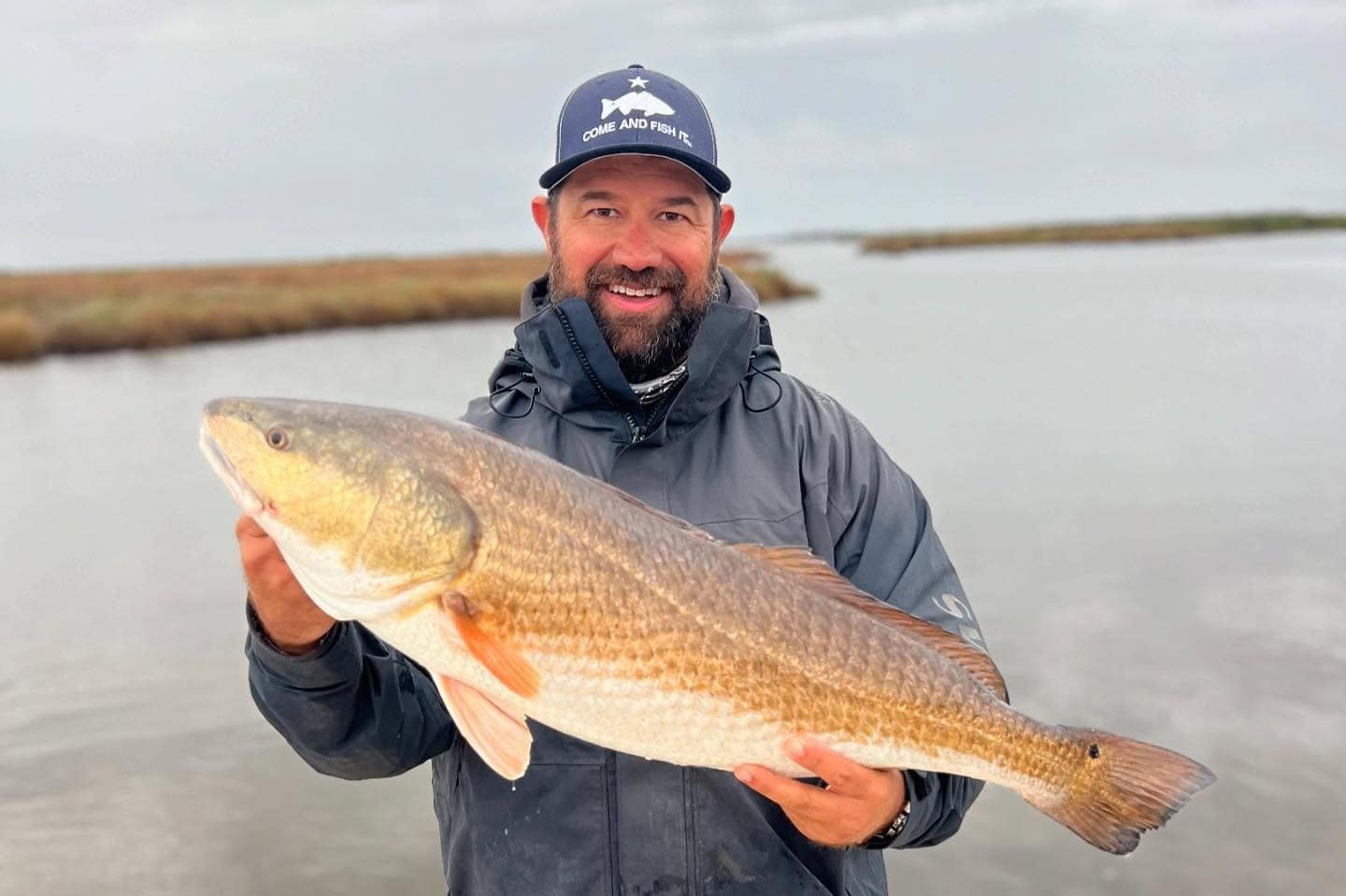 A man smiling and holding up a redfish while on a fishing charter.