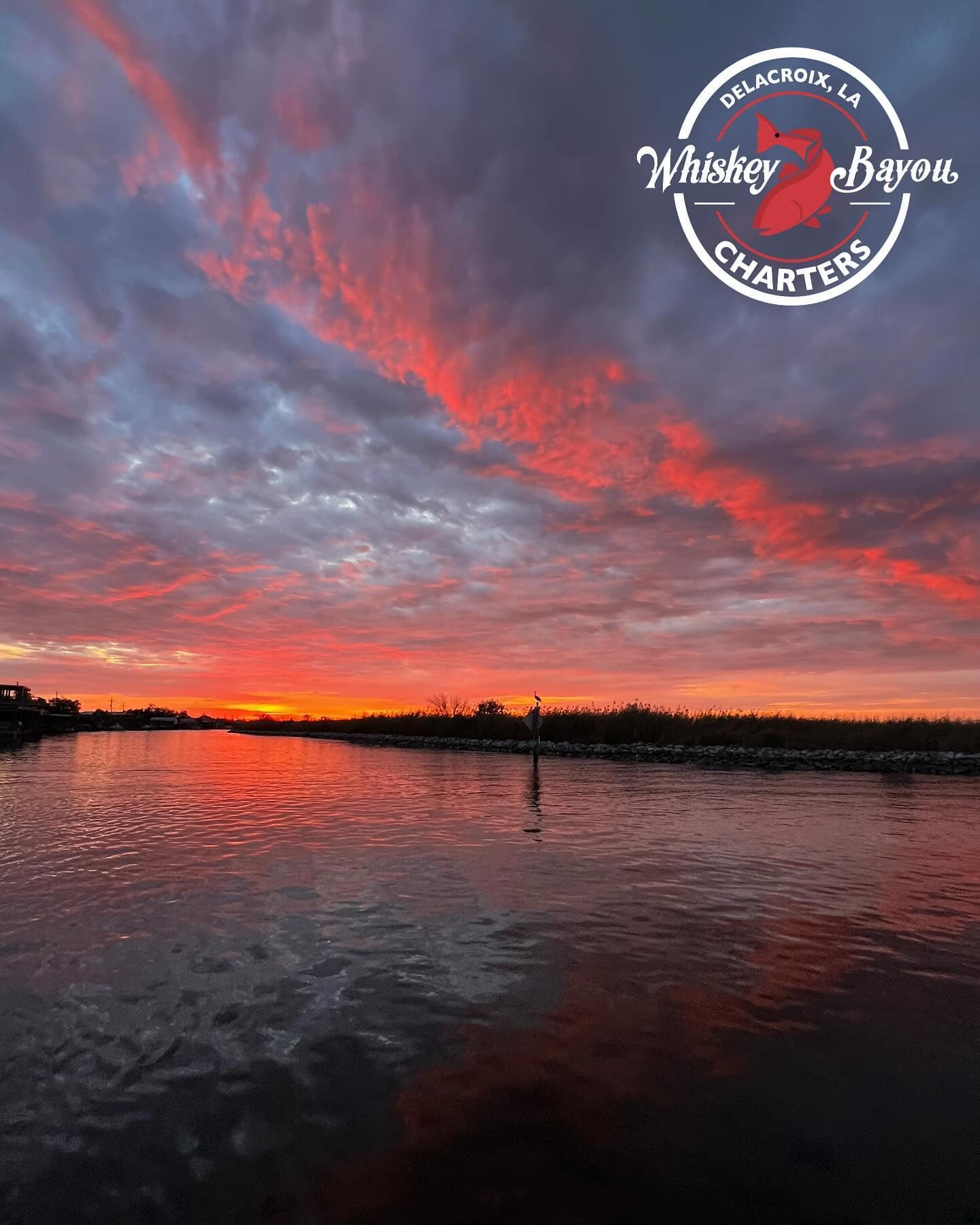 Stunning sunrise over the marsh waters of Delacroix, Louisiana, with vibrant red and orange clouds reflecting on the water.