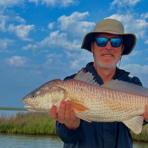 Man holding a redfish he caught while fishing with Whiskey Bayou Charters.