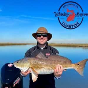 Man holding up a redfish from summer fishing in delacroix.