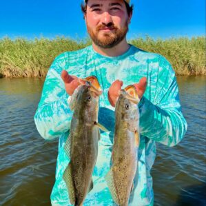 Man on a fishing charter holding up two speckled trout.