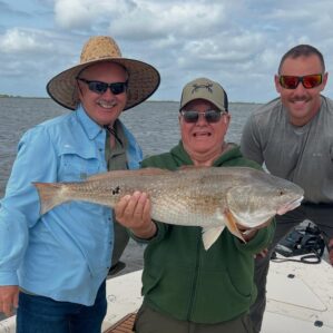 Three men holding a redfish caught while summer fishing in Louisiana.