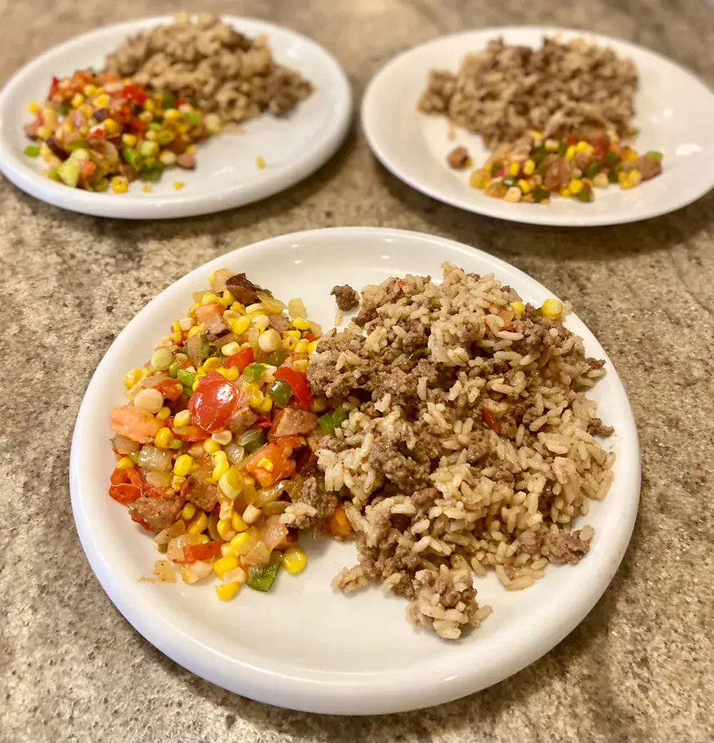 Three white plates, each filled with dirty rice and Corn Maque Choux.