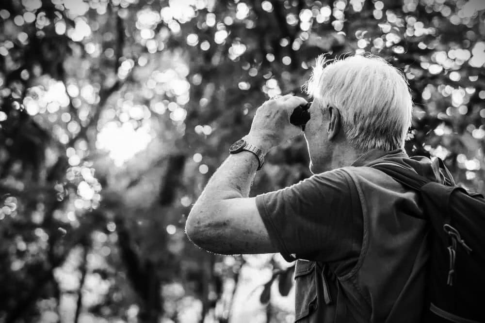 Black and white photo of a man with binoculars looking into the forrest