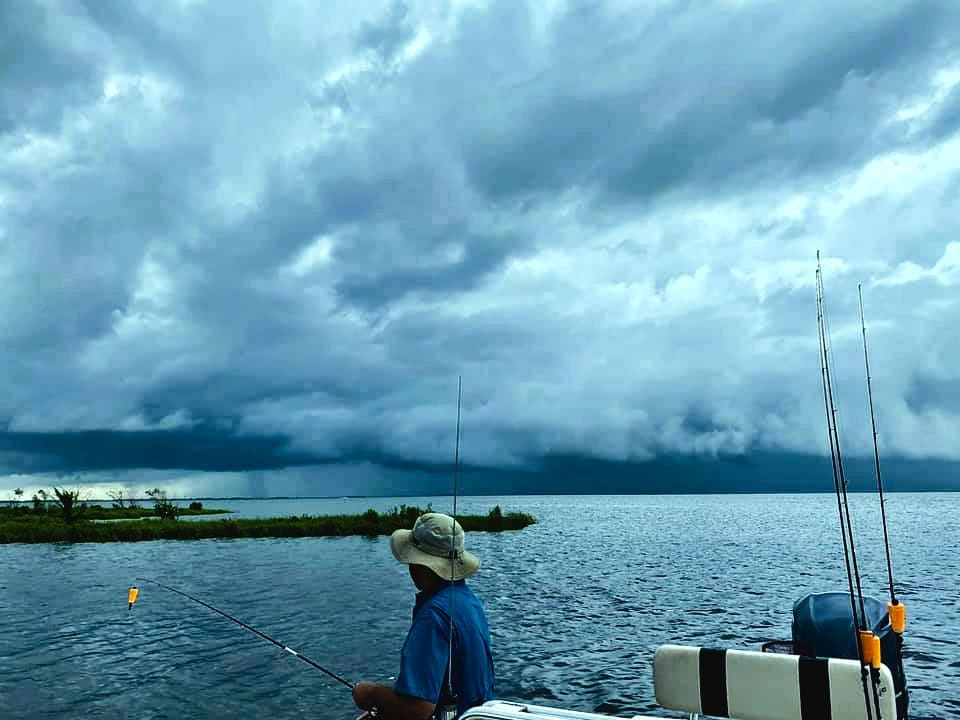 Angler fishing on the water while great gray clouds loom overhead