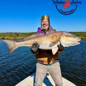 A very happy man wearing a golden, brimless cap, holds a huge fish up for the camera.