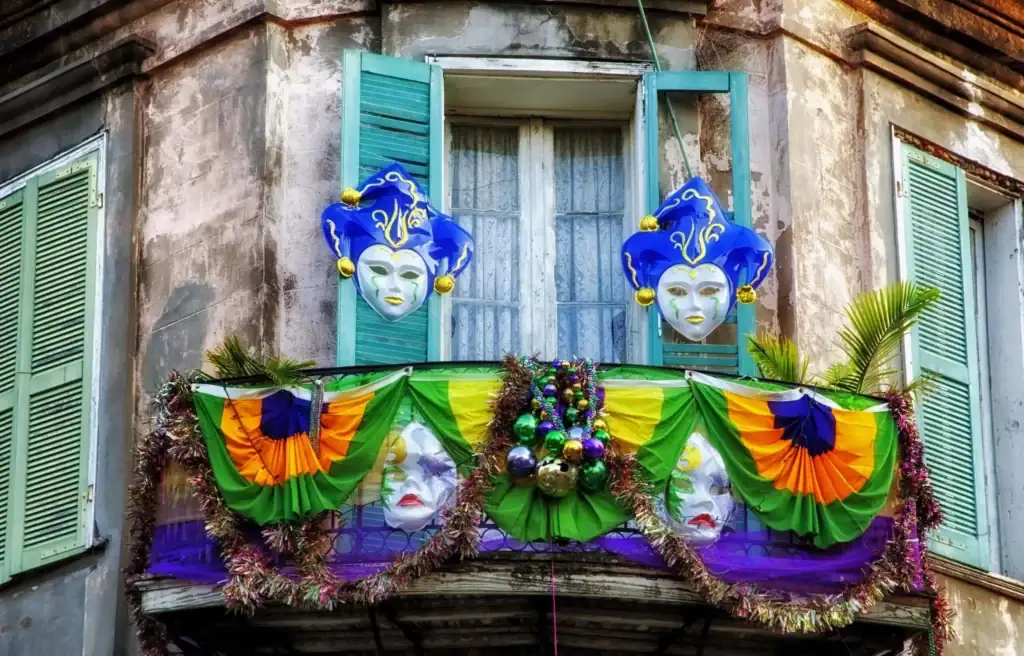 Exterior view of a Bourbon Street balcony decorated with Mardi Gras colors and masks.