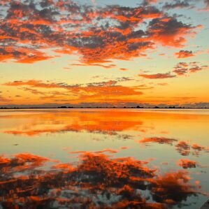A beautiful sunrise painting the clouds and sky above and water below in rich pinks, oranges, and yellows.